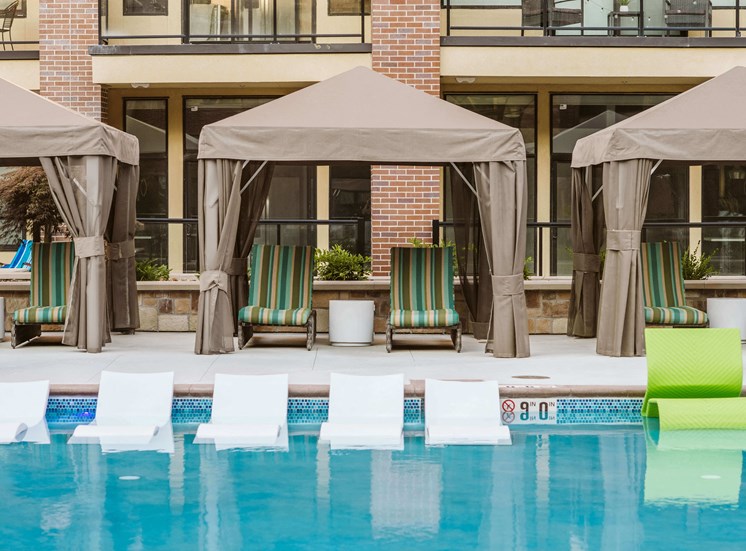chaise lounge chairs under a canopy by an outdoor pool